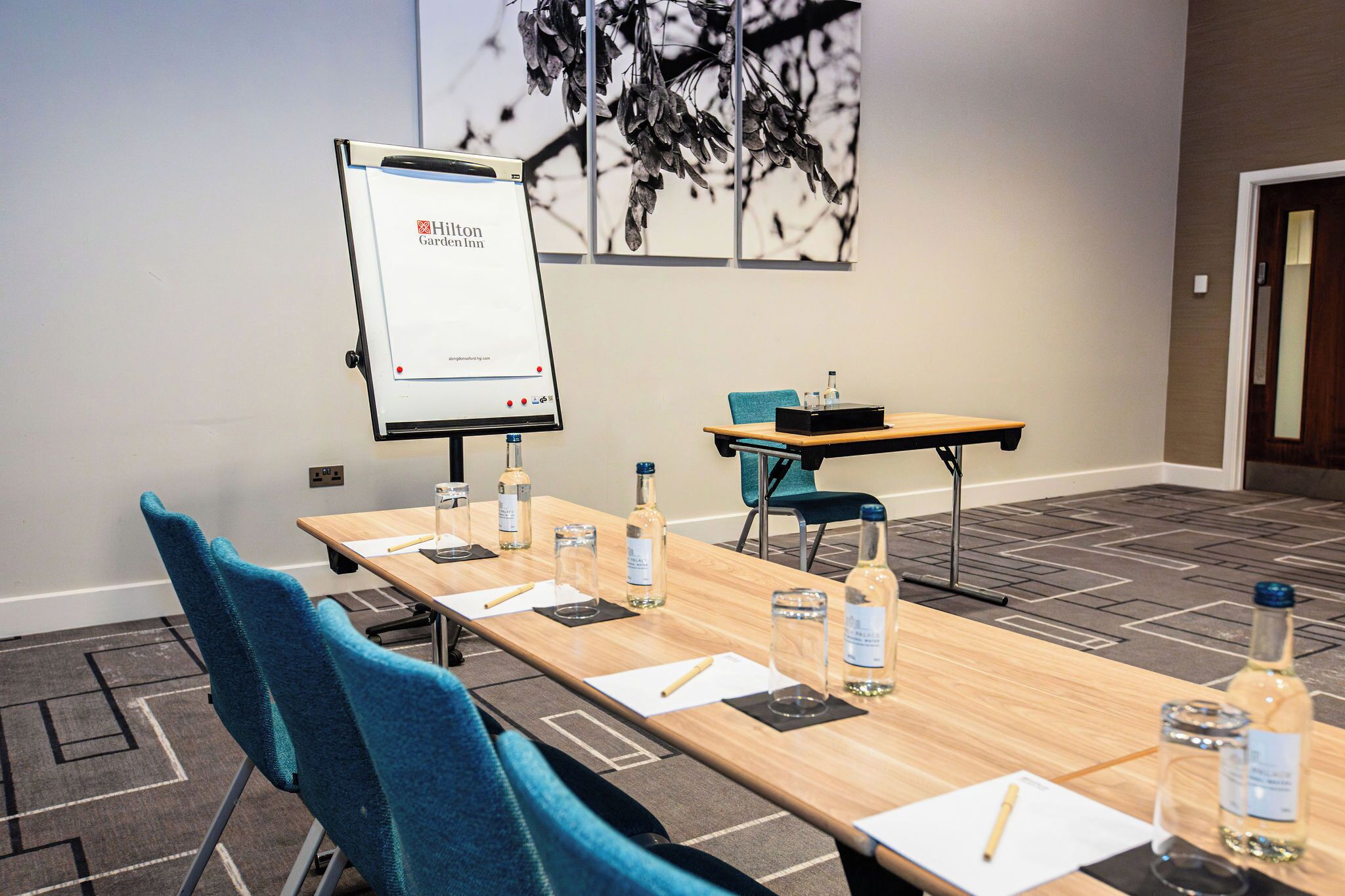 A conference room with a long table, blue chairs, a whiteboard, and a projector screen displaying "Hilton Garden Inn".