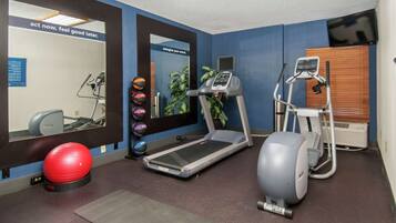A fitness room with a treadmill, elliptical, and exercise balls.
