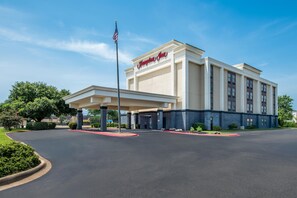 Un hotel Hampton Inn con entrada techada, bandera y cielo despejado.