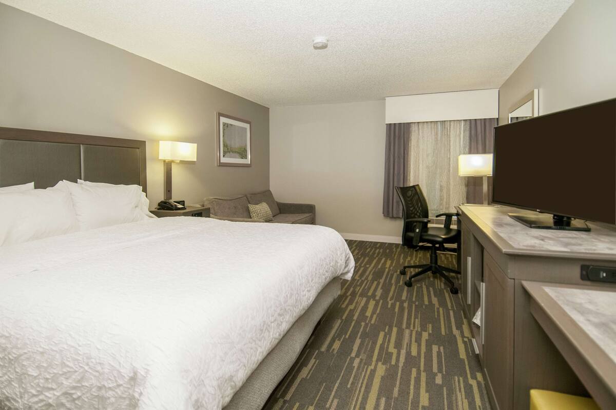 A hotel room with a large bed, a desk with a computer, a chair, a lamp, and a television.