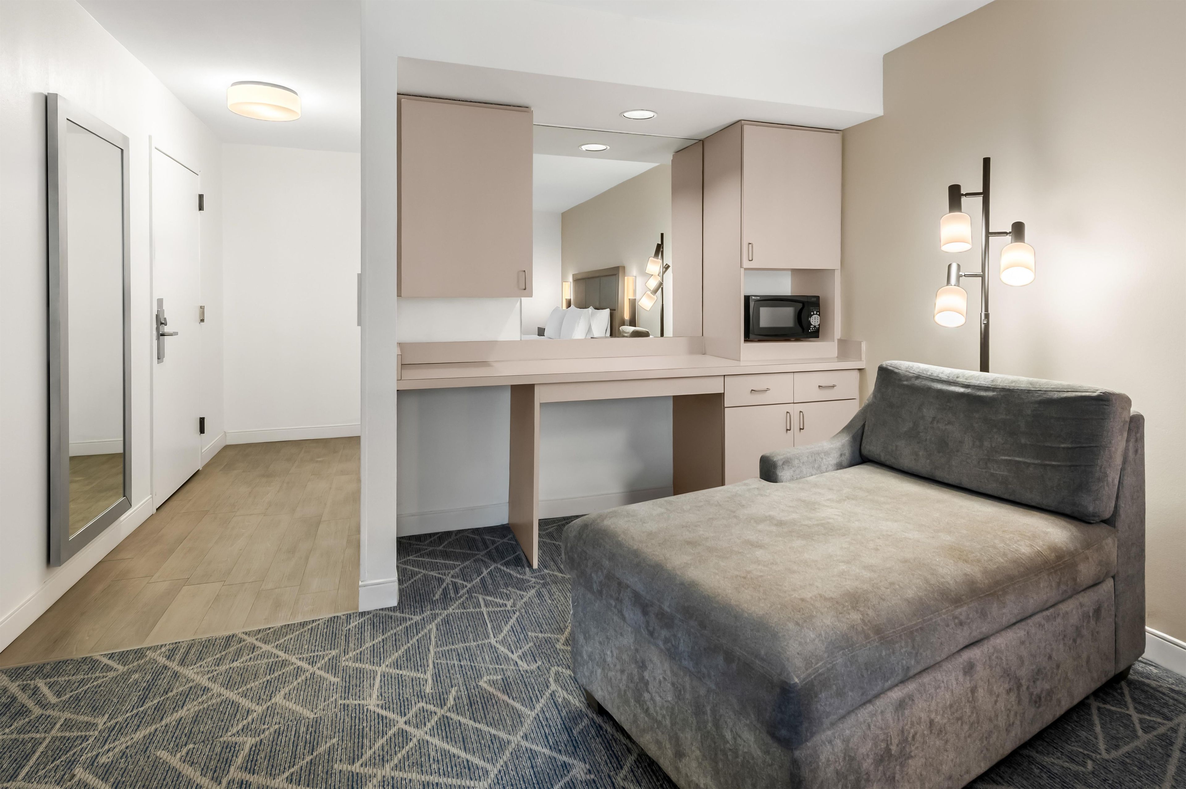 A modern hotel room with a sofa, a desk, a microwave, and a large mirror.