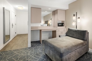 Una habitación de hotel moderna con sofá, escritorio, microondas y un espejo grande.