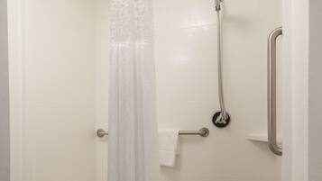 A shower with a white curtain, a handheld showerhead, a grab bar, and a white bench.