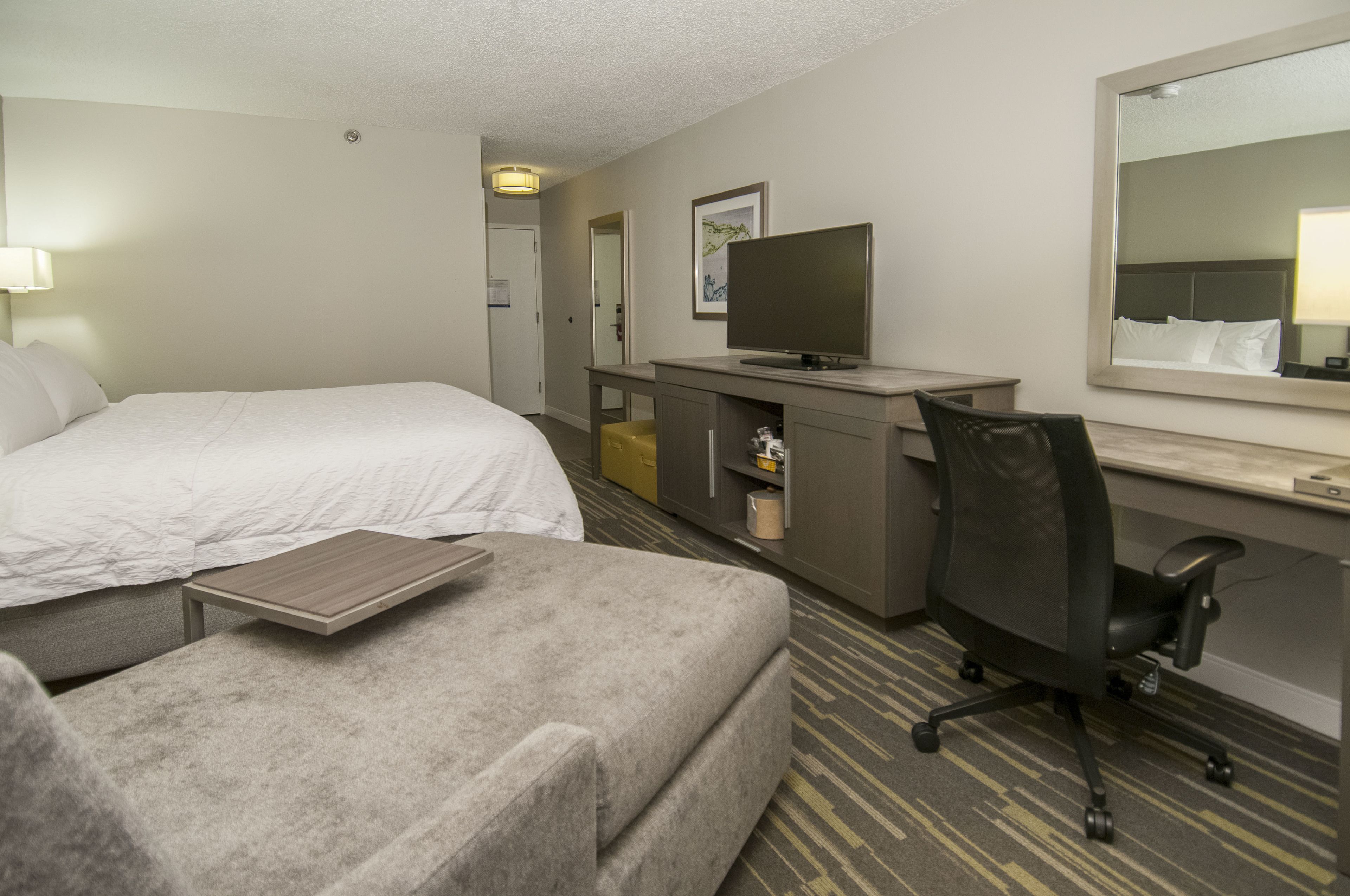 A hotel room with a bed, a desk, a chair, a television, and a mirror.