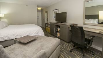 A hotel room with a bed, a desk, a chair, a television, and a mirror.