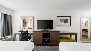 A hotel room with a bed, a desk with a flat-screen TV, a chair, a small sofa, and a mirror.
