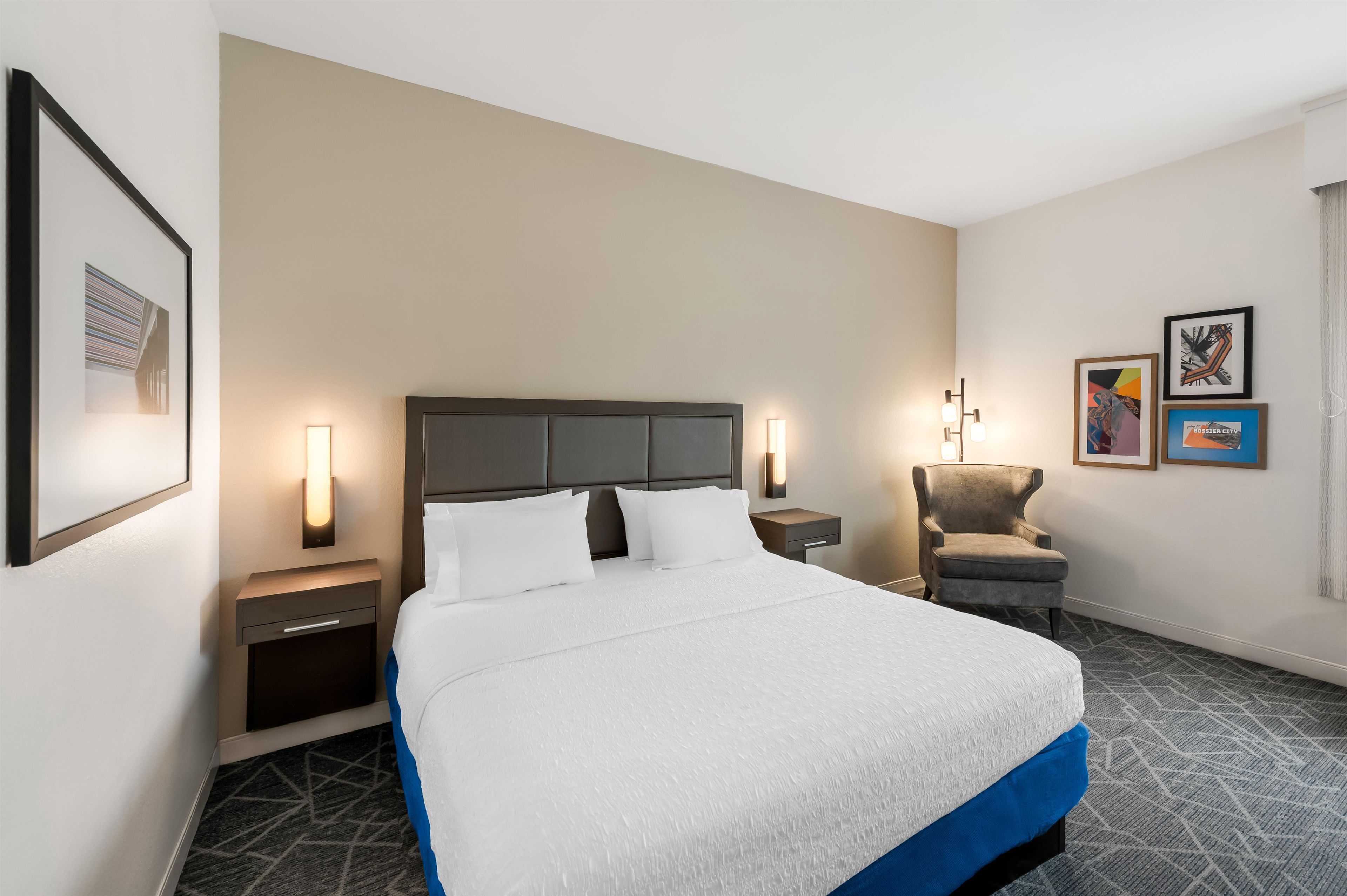 A hotel room with a large bed, two bedside tables, a chair, and artwork on the walls.