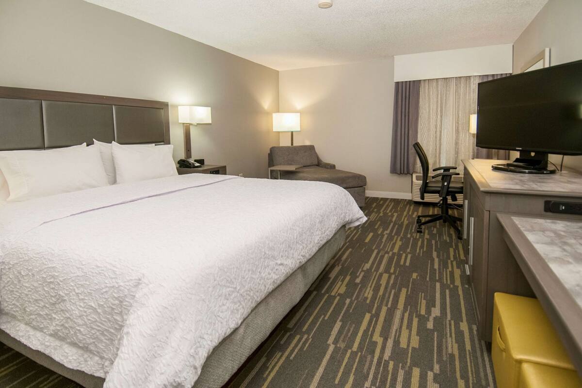 A hotel room with a large bed, a desk with a computer, a chair, and a television.