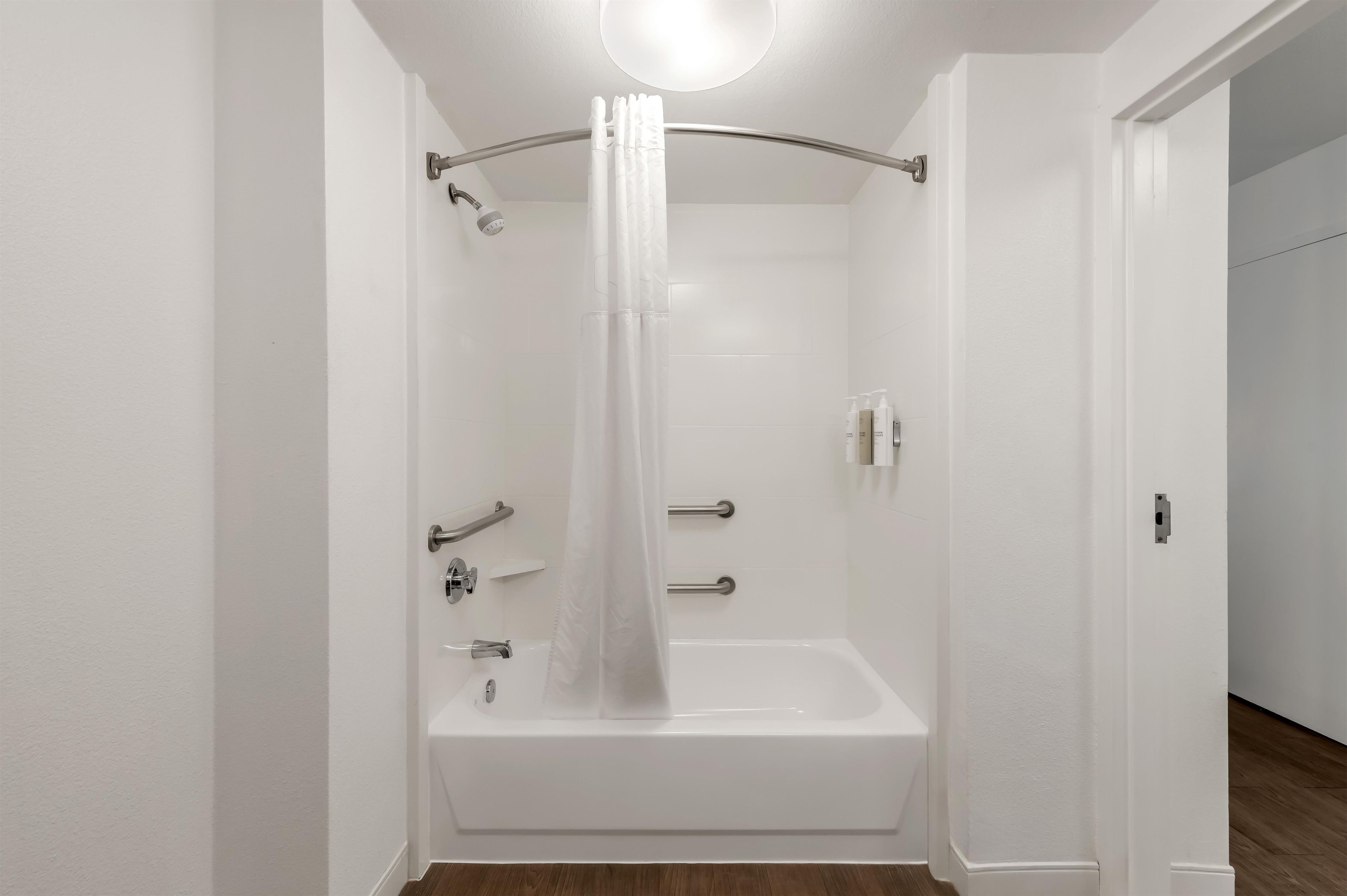 A modern bathroom with a bathtub, shower, and handrails.