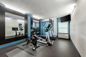 Un gimnasio con equipo de ejercicio, un espejo grande y carteles motivacionales.