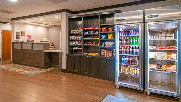 Un hall de hotel con una recepción, una estantería y dos vitrinas refrigeradas.