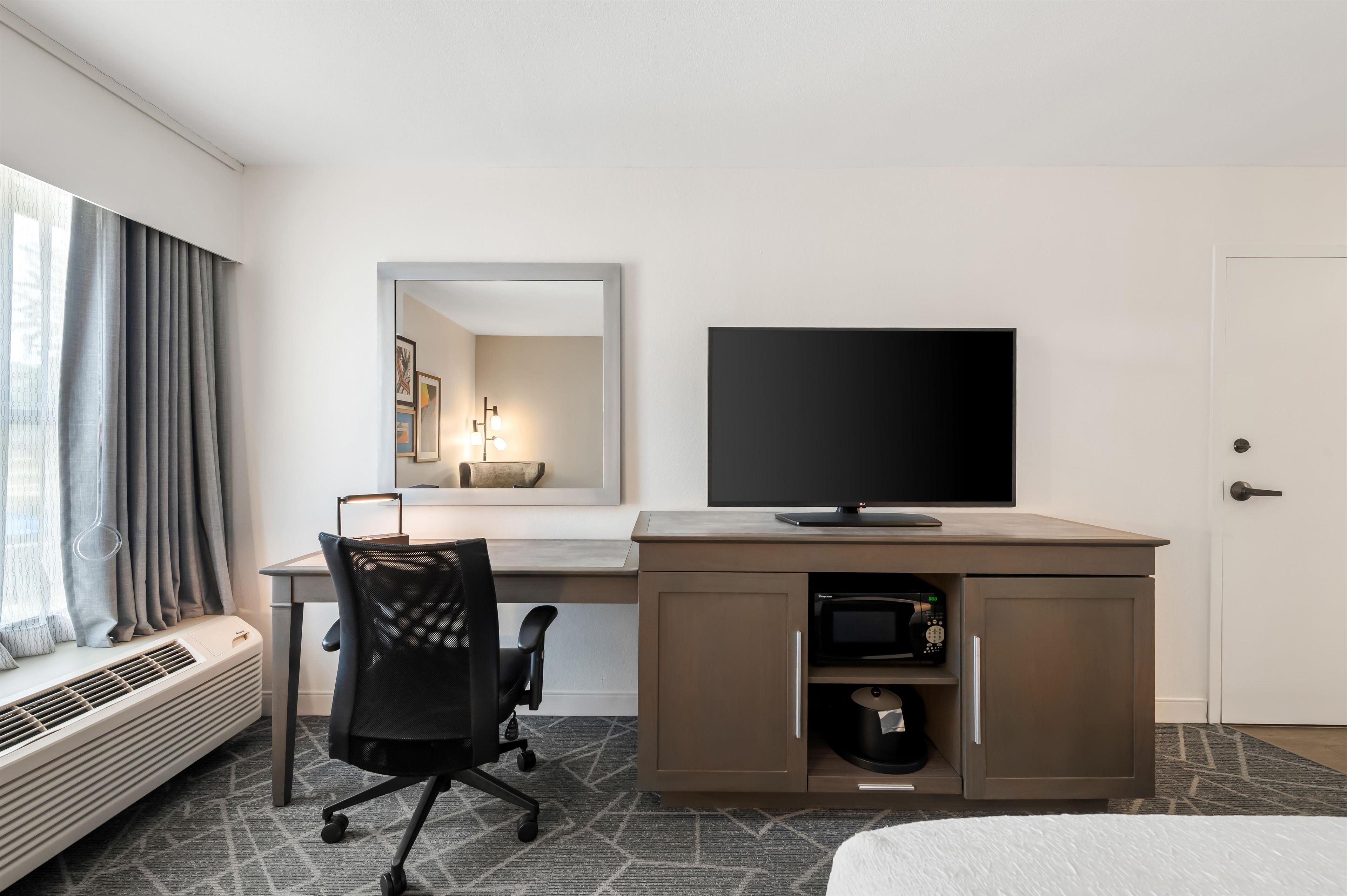 A hotel room with a desk, chair, flat-screen TV, built-in microwave, and a bed.