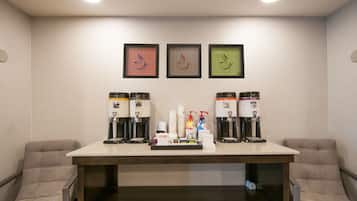 A hotel room with a coffee station, framed artwork on the wall, and two cushioned chairs.