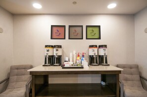 Habitación de hotel con estación de café, cuadros en la pared y dos sillones acolchados.