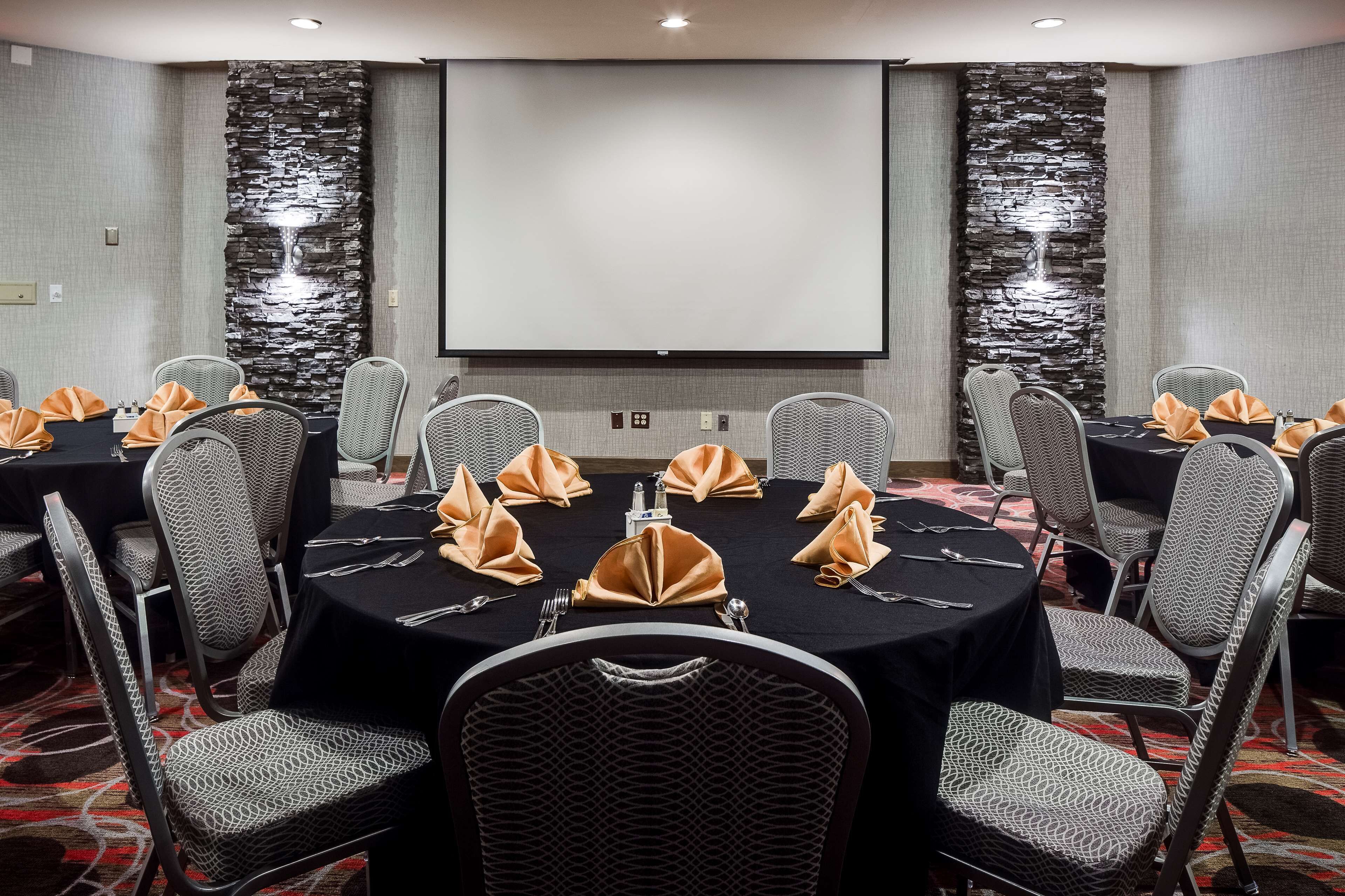 Un salón de conferencias con mesas redondas, sillas grises con estampado y una pantalla grande.