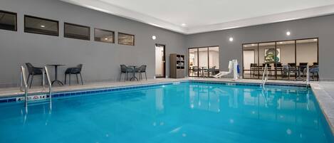 Una piscina interior con agua cristalina y azul, rodeada de sillones y mesas.