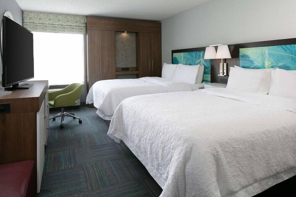 A hotel room with two beds, a TV, a desk, and a chair.