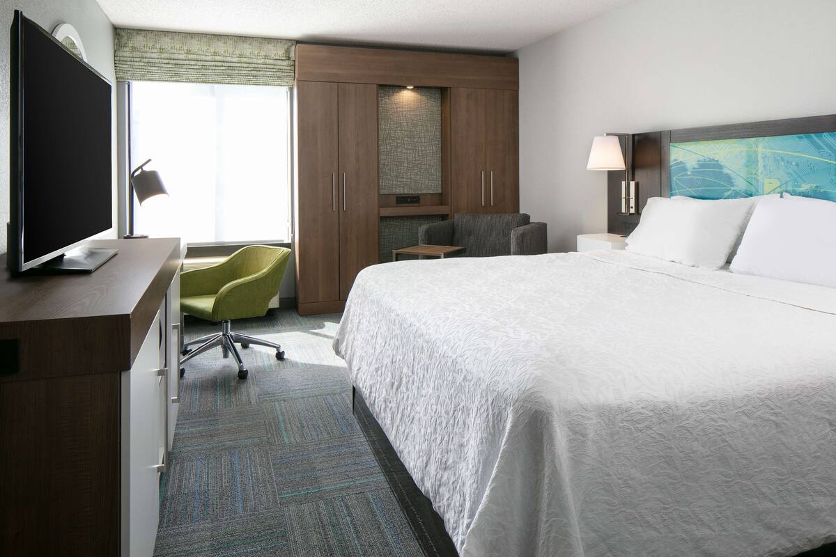 A hotel room with a large bed, a desk with a computer, a green chair, and a TV.