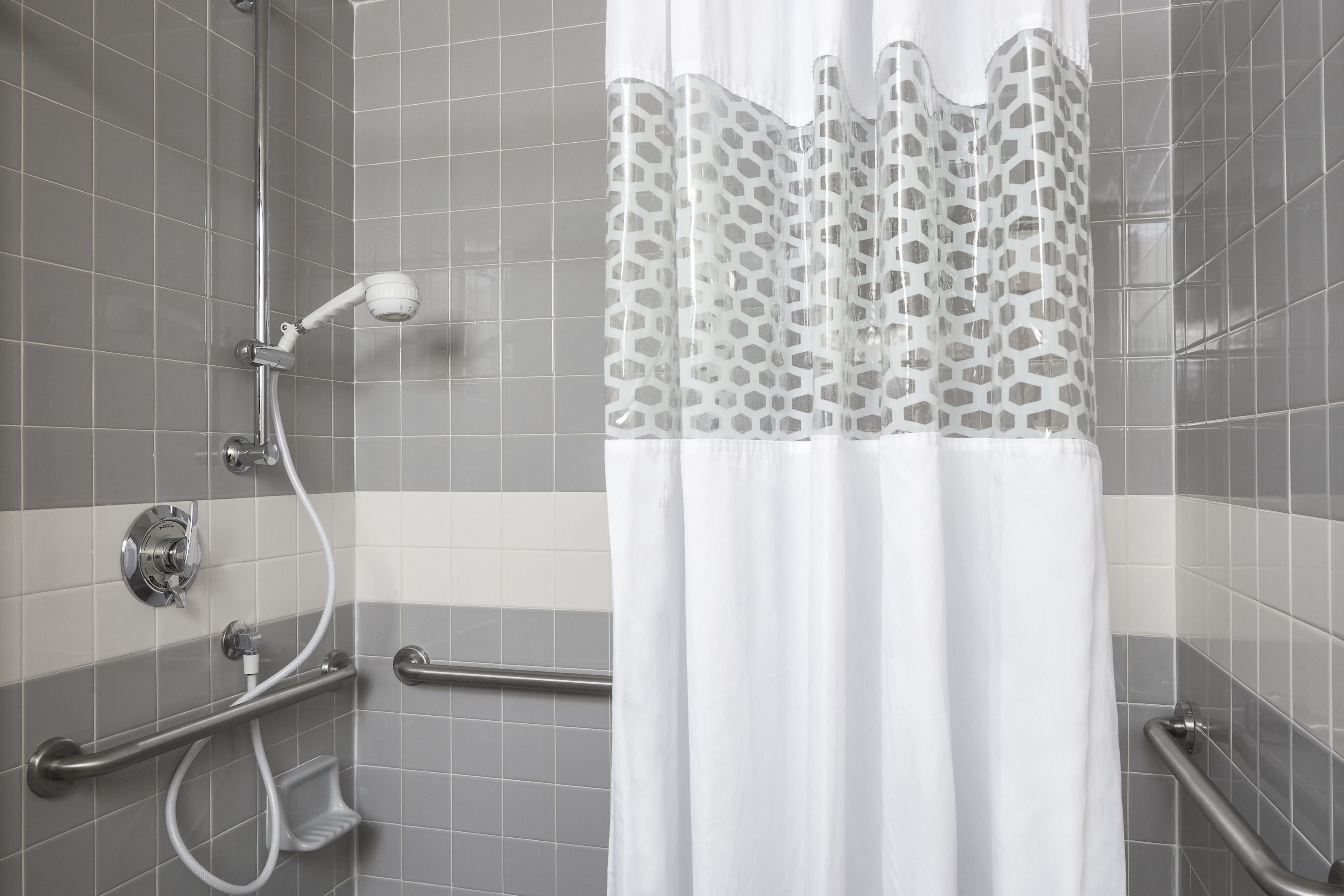 A shower area with a white curtain, grab bars, and a handheld showerhead.