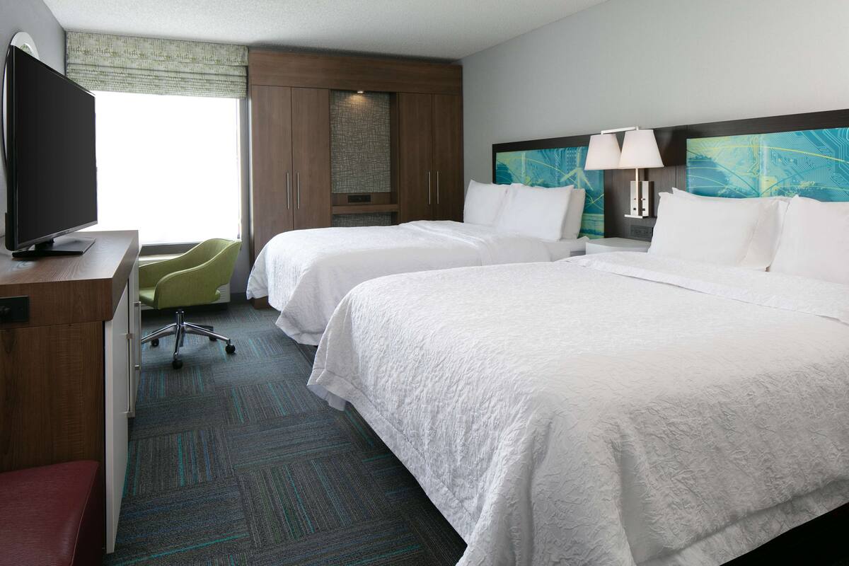 A hotel room with two beds, a TV, a desk, and a chair.