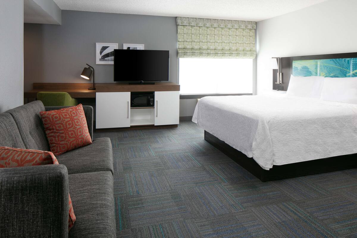 A hotel room with a bed, a sofa, a desk with a TV, and a window with a view.