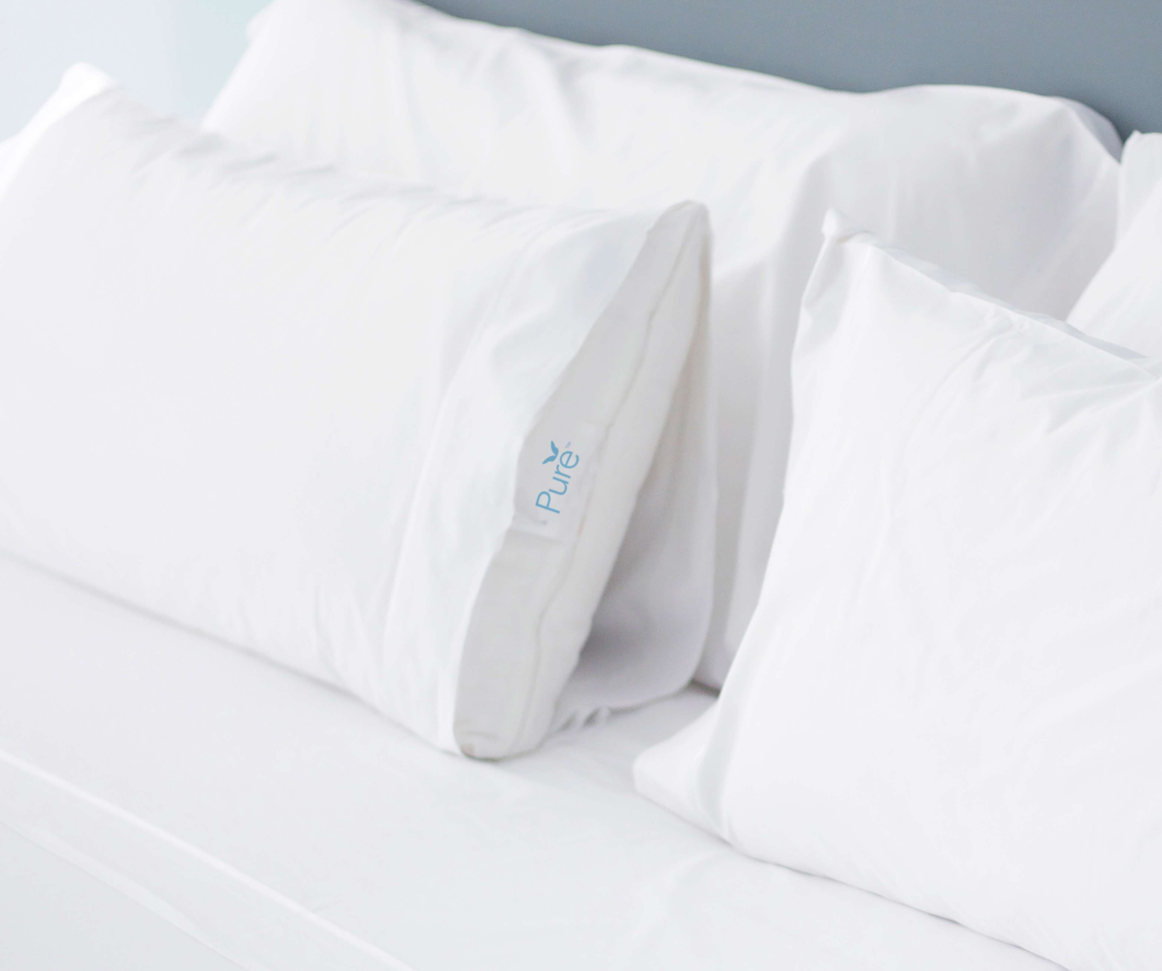Un lit blanc avec des oreillers, dont l’un porte le logo « Pure ».