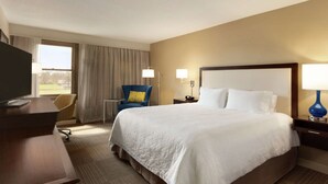 A hotel room with a large bed, a desk with a TV, a chair, and two bedside lamps. - Hampton Inn & Suites Springdale (Springdale)