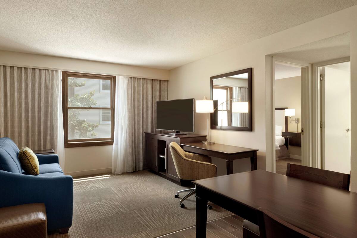 A hotel room with a large bed, a desk with a chair, a television, and a window with curtains.