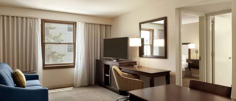 A hotel room with a large bed, a desk with a chair, a television, and a window with curtains.