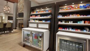 A hotel lobby with a seating area, a fireplace, and shelves stocked with snacks and beverages. - Hampton Inn & Suites Springdale (Springdale)