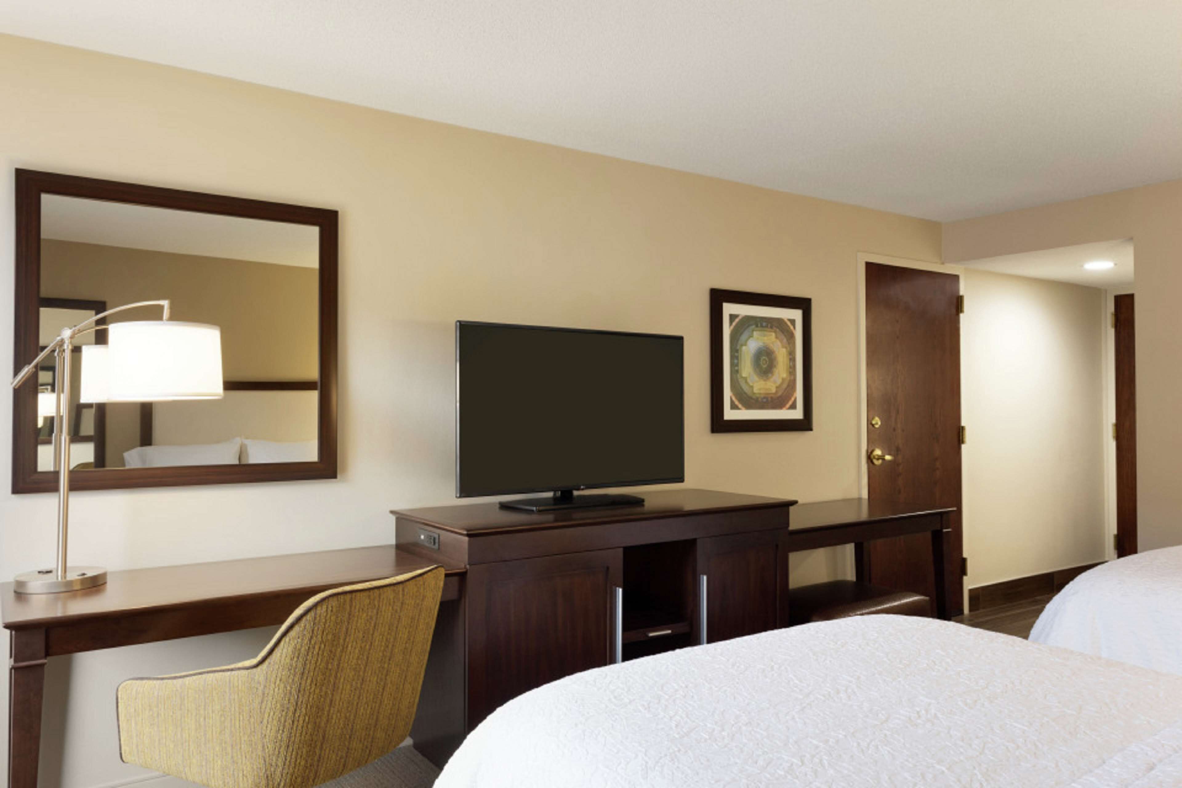 Une chambre d’hôtel avec un lit, un bureau, une chaise, une télévision, un miroir et une porte.