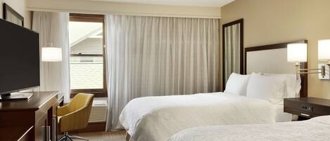 A hotel room with two beds, a desk with a TV, a chair, and a window with curtains.