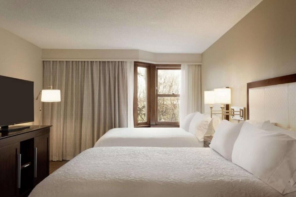 A hotel room with two beds, a TV, a desk, and a window with curtains.