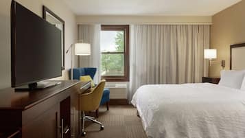 Une chambre d’hôtel comprenant un lit, un bureau avec une télévision, une chaise, une fenêtre avec des rideaux et une lampe.