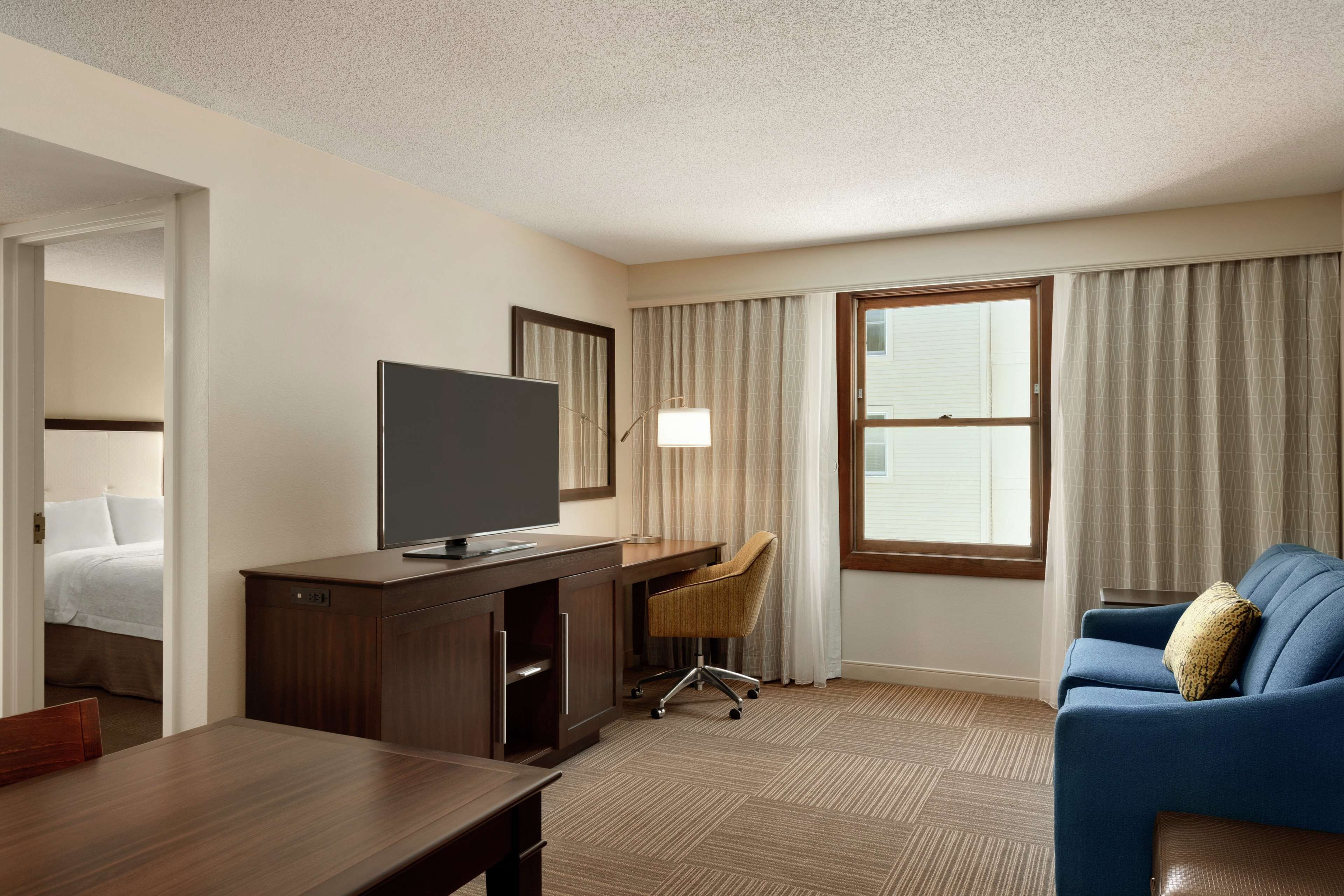 A hotel room with a wooden desk, a television, a blue sofa, and a window with curtains.