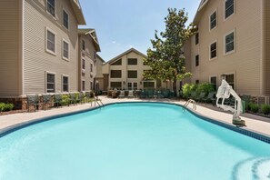 A swimming pool surrounded by buildings with a patio area and outdoor seating.