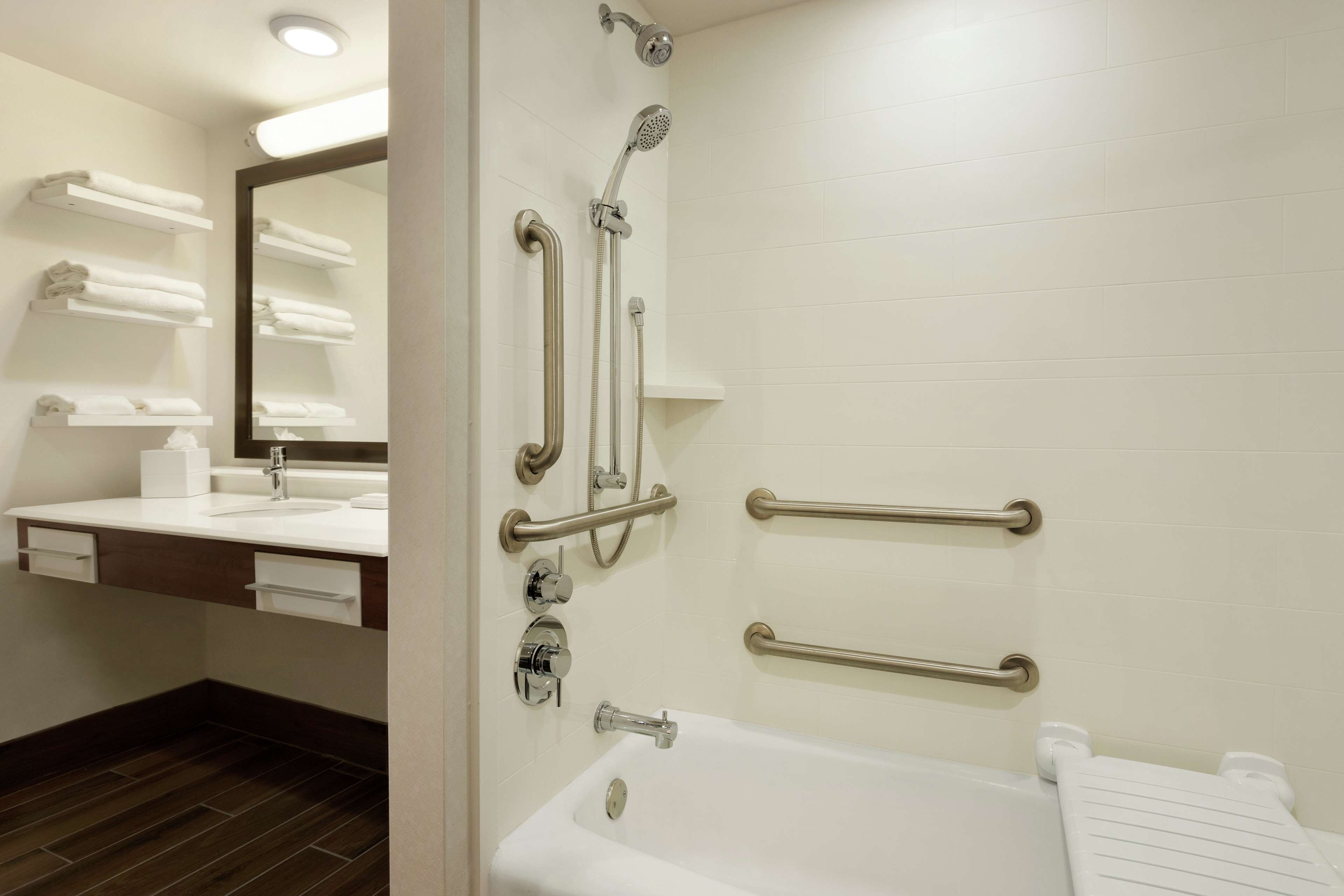 Een moderne badkamer met een witte badkuip, een grote spiegel en handgrepen voor toegankelijkheid.
