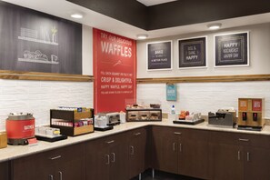 A breakfast bar with waffle stations, a coffee machine, and a sign promoting waffles. - Hampton Inn Youngstown/Boardman (Poland)