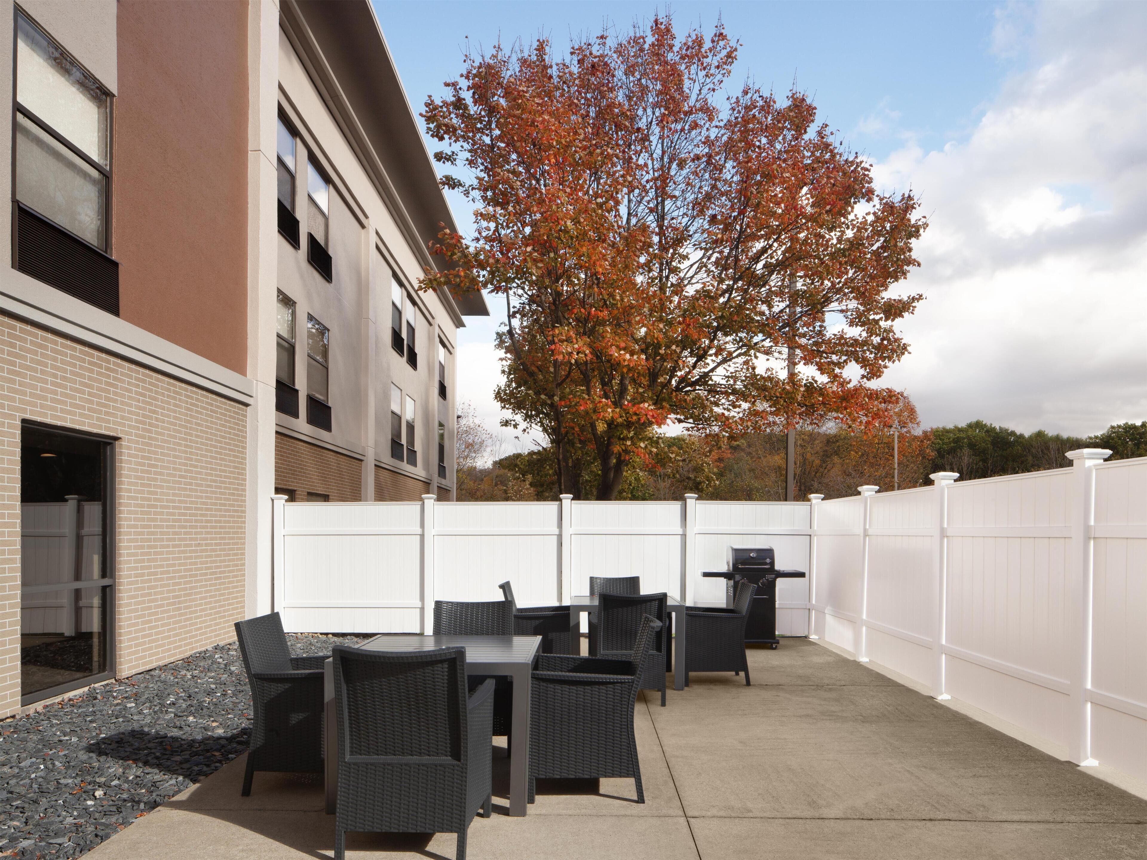 Une terrasse extérieure avec des tables et des chaises, une clôture blanche et un bâtiment doté de fenêtres et d’un mur en briques.