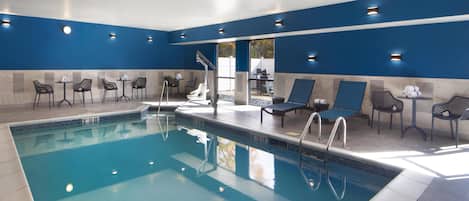 A swimming pool with lounge chairs and tables, surrounded by blue walls and recessed lighting.