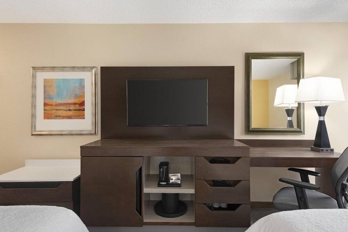 Una habitación de hotel con una cama, un escritorio con televisor de pantalla plana, una cafetera, un espejo y una lámpara.