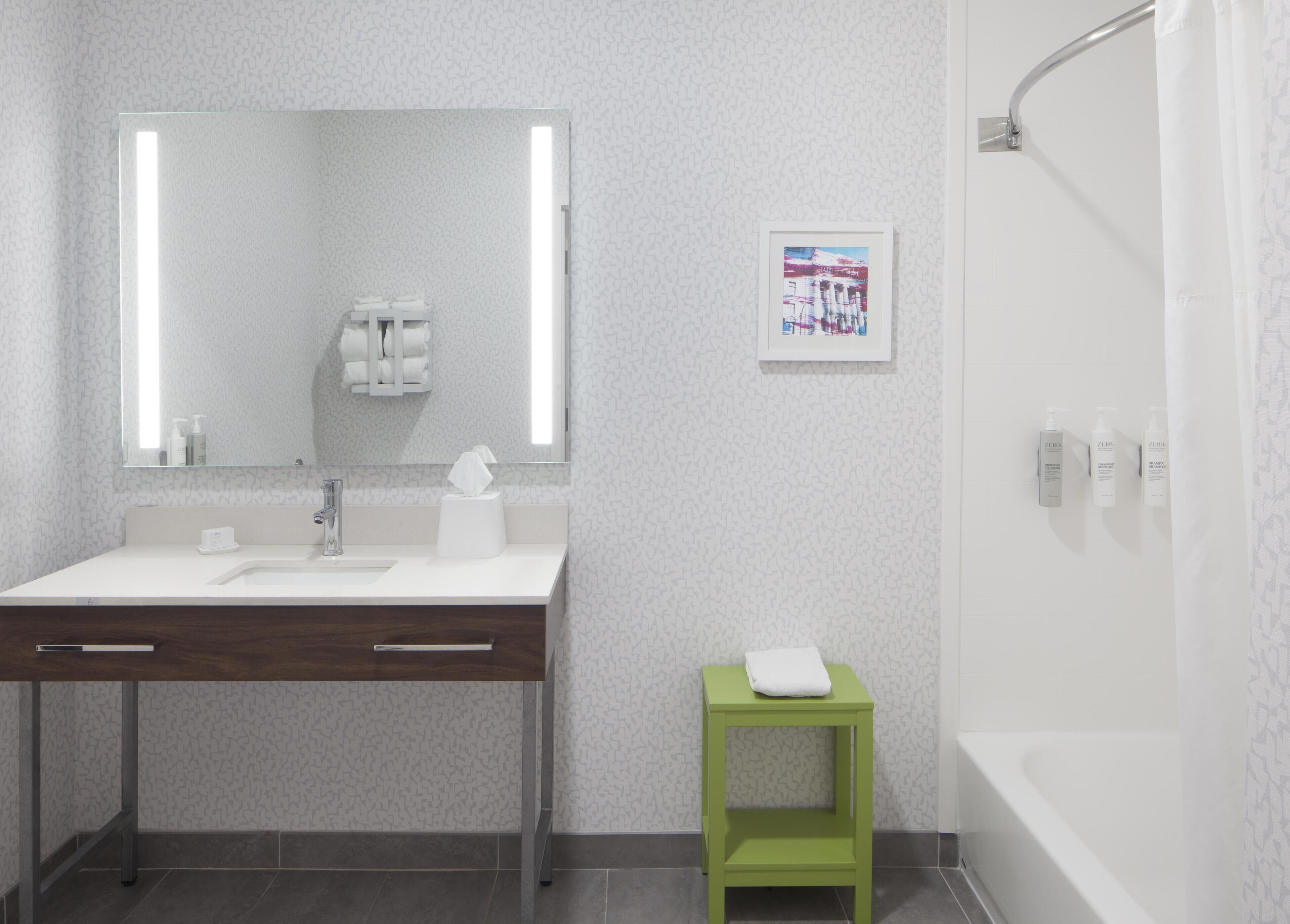 Une salle de bain moderne avec un lavabo blanc, un miroir, un tabouret vert et un rideau de douche.