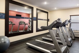 Un gimnasio con cintas de correr, una bicicleta estática y una pelota grande de ejercicios.