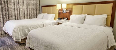 A hotel room with two beds, a bedside table with a lamp, and a patterned curtain.