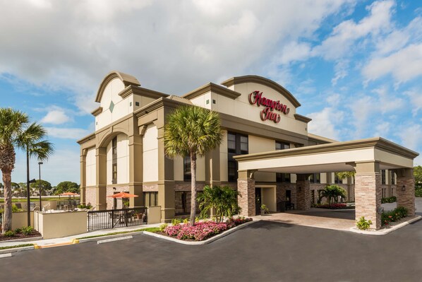 A hotel with a covered entrance, palm trees, and a clear sky.