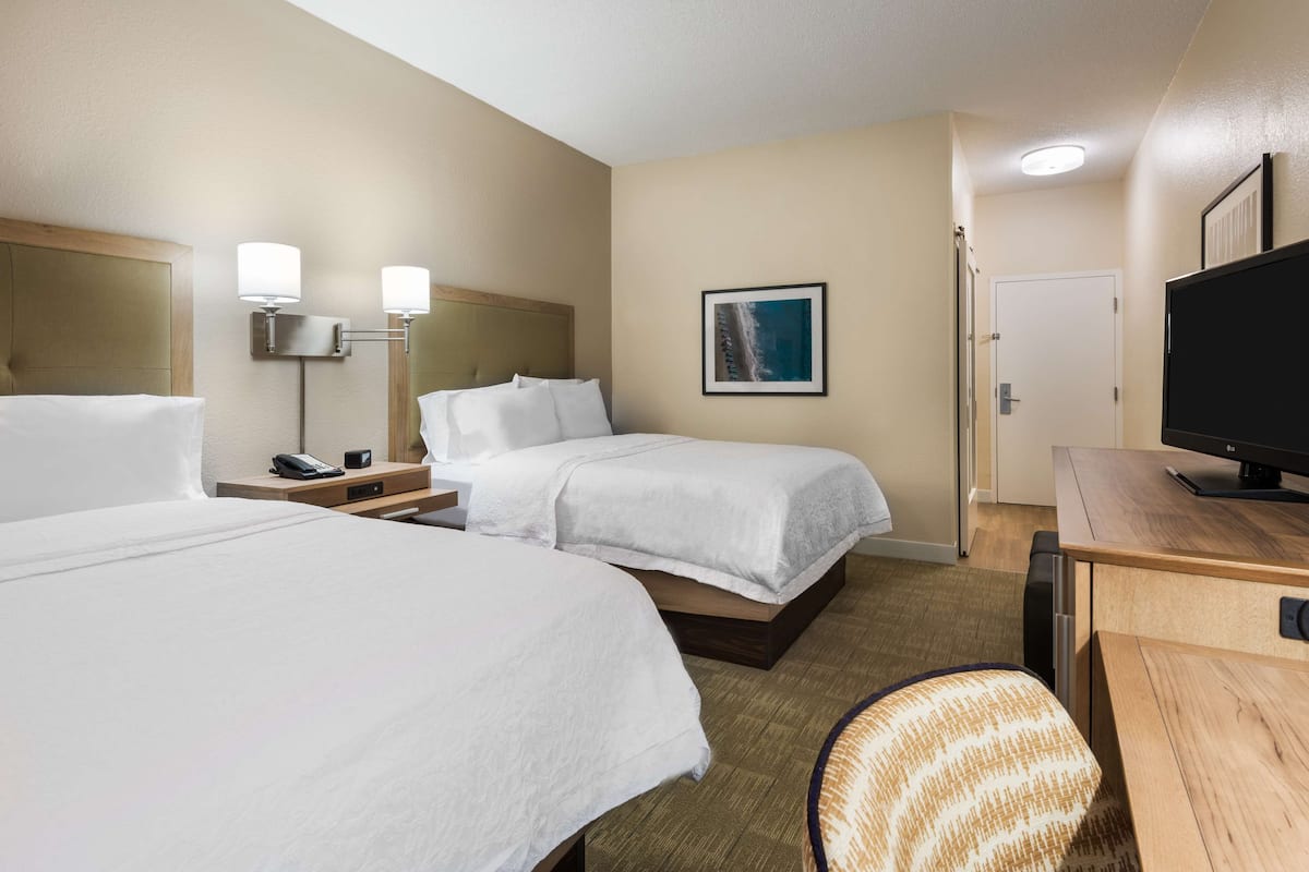 A hotel room with two beds, a desk, a chair, a TV, and a framed picture on the wall.