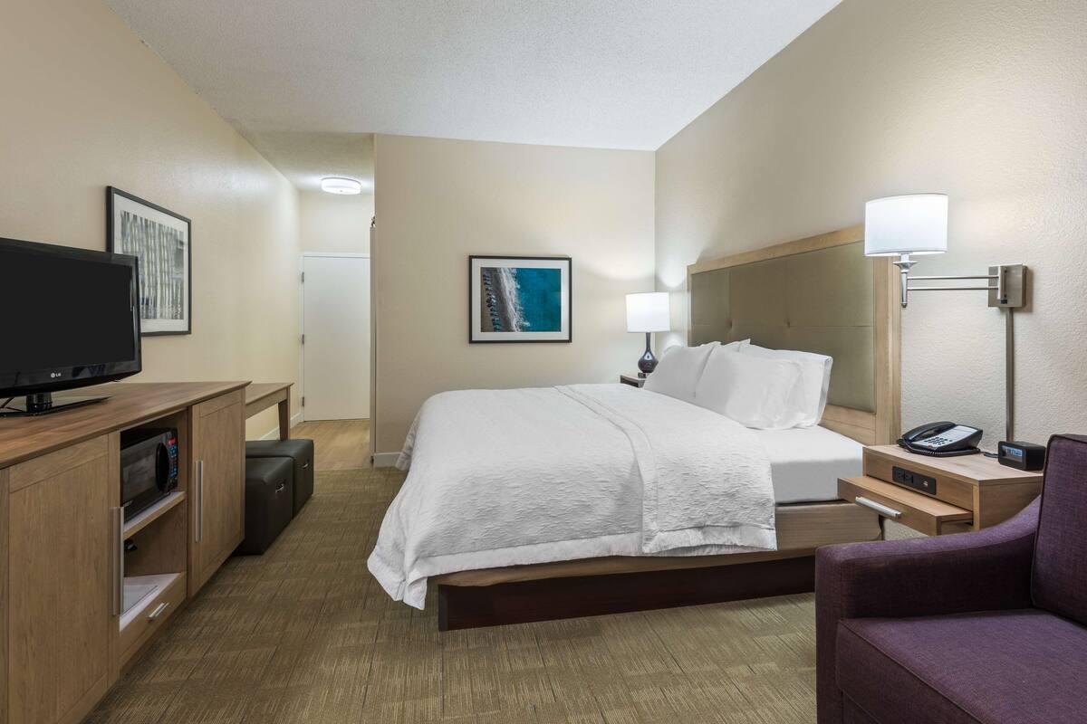 A hotel room with a bed, a television, a desk with a lamp, and a chair.