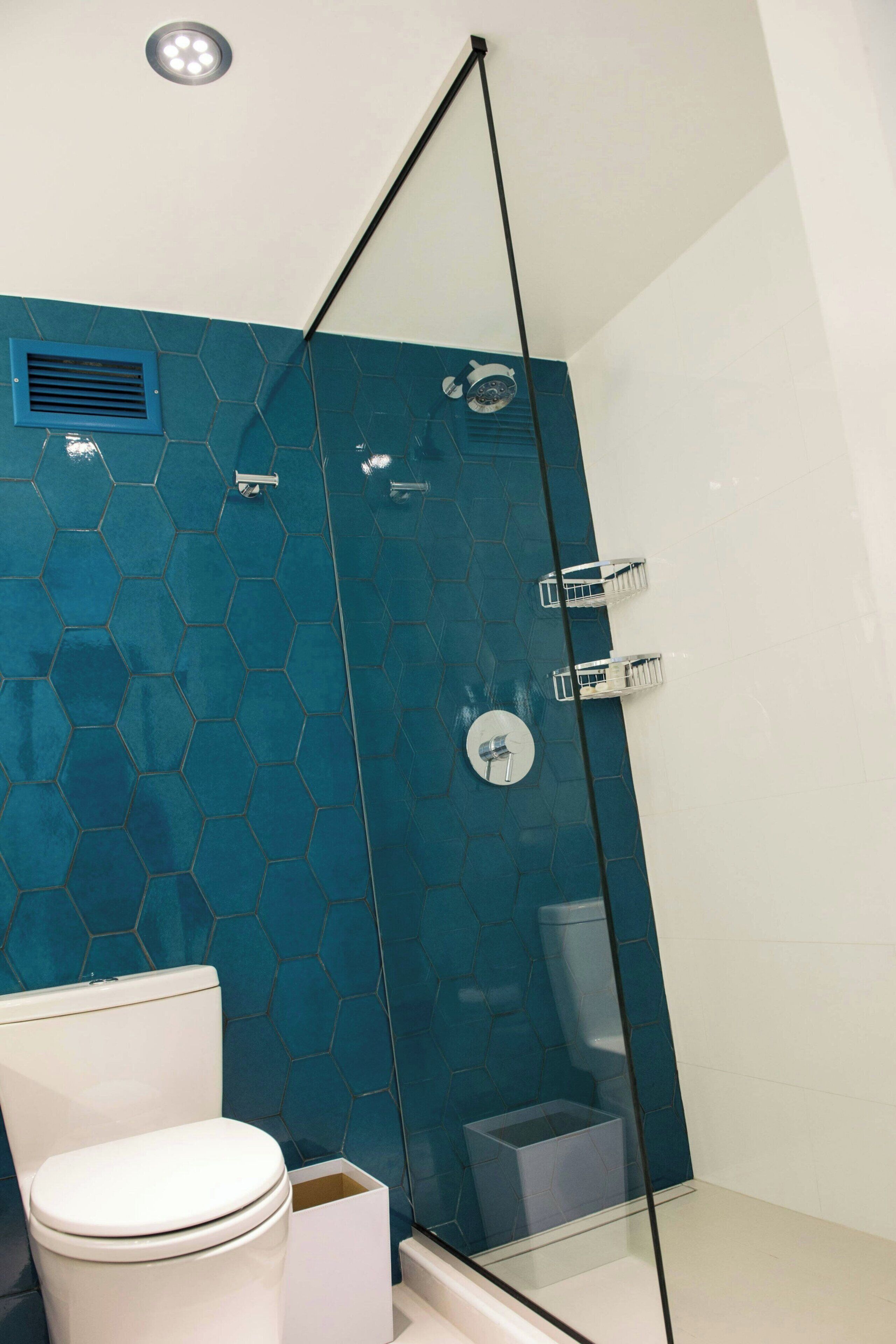 A bathroom with a glass-enclosed shower, a white toilet, and a blue hexagonal tile wall.
