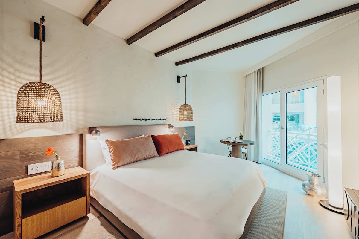 A modern bedroom with a large bed, wooden headboard, and pendant lights.