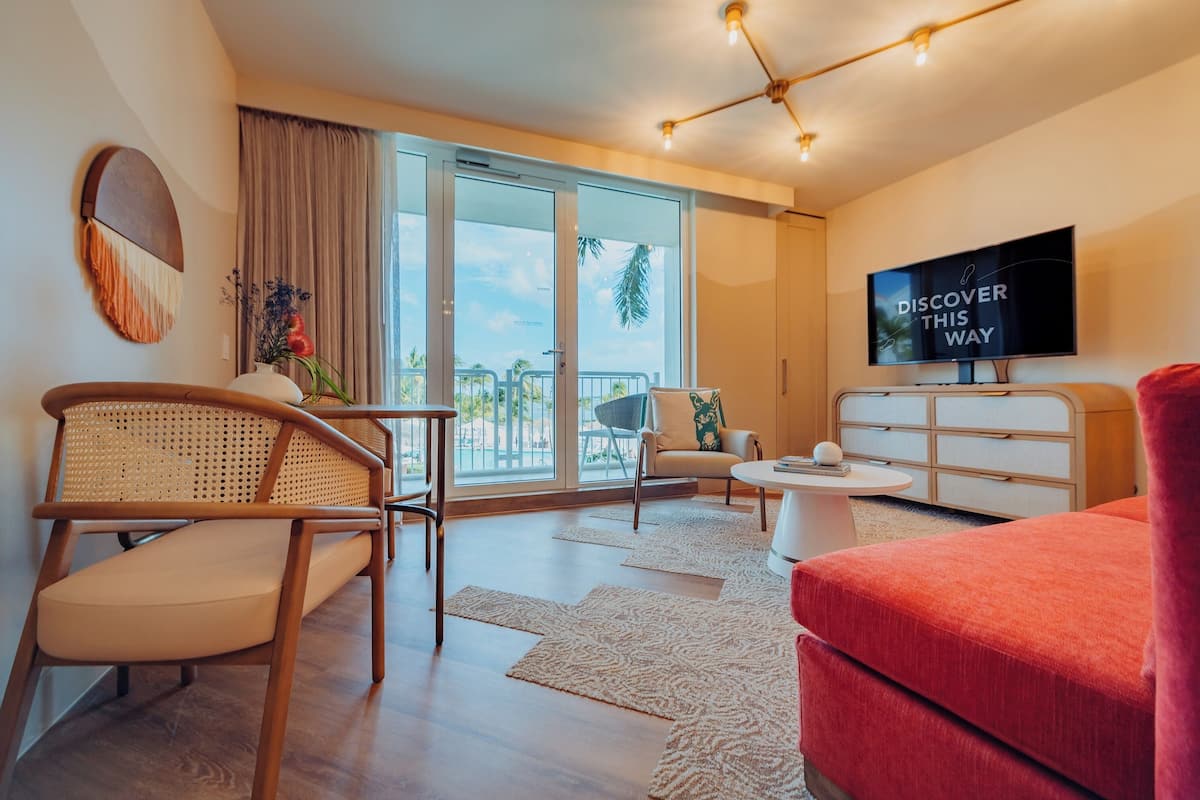 A modern living room with a sofa, chairs, a TV, and a balcony with curtains.
